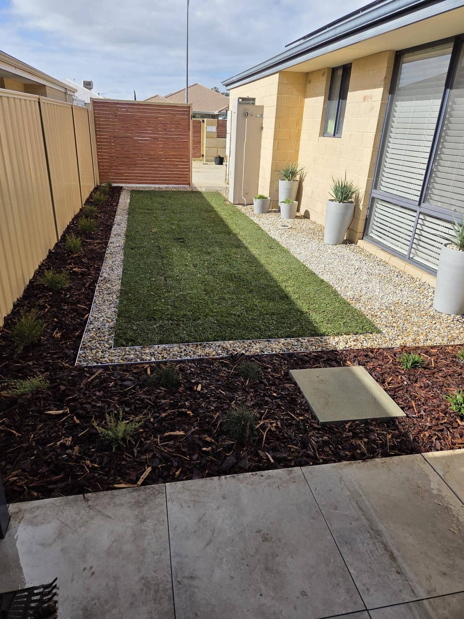 Side yard landscaping with turf, pebbles and planters